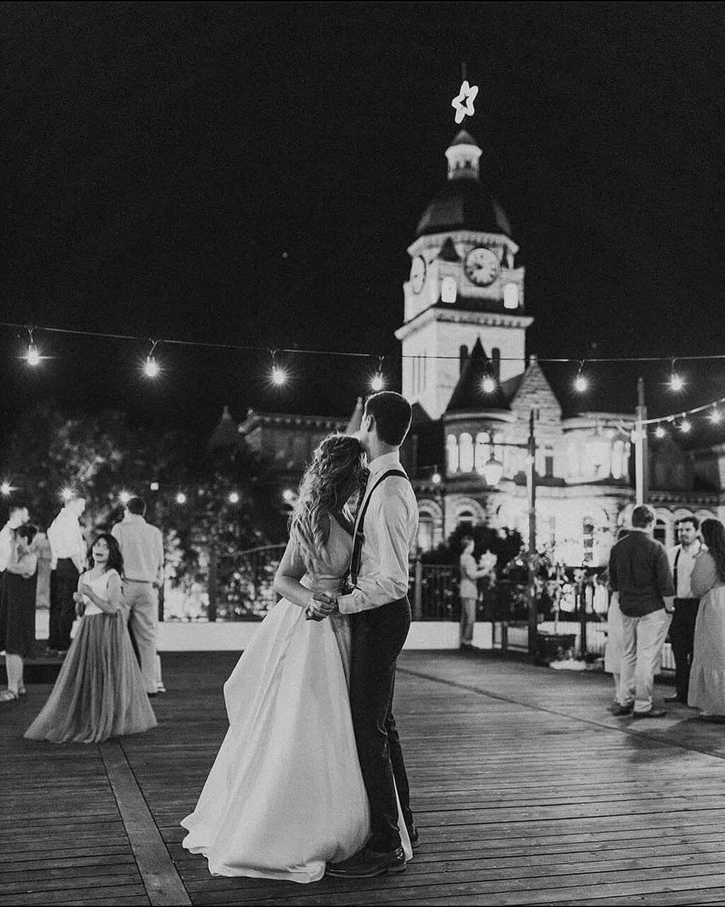 Bride and groom dance on the rooftop at night under string lights